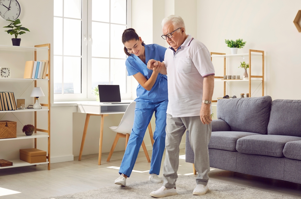 Young,Nurse,Helping,Elderly,Man,Walk,In,The,Room,,Holding